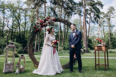 Düğün kemerinin yanında poz veren mutlu gelin ve damat parktaki düğün töreninde            