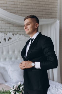 Sabahları yatak odasında zarif bir takım elbise giyen yakışıklı damadın portresi.