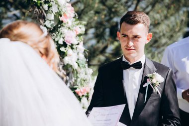 Güzel, mutlu gelin ve damat, düğün günlerinde çiçek kemerinin yanında.    