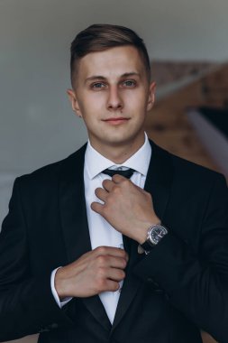 Siyah takım elbiseli ve kravatlı, kameraya gülümseyen yakışıklı bir gencin portresi.