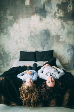 Stüdyo odasında yatakta poz veren genç mutlu anne ve kız. 