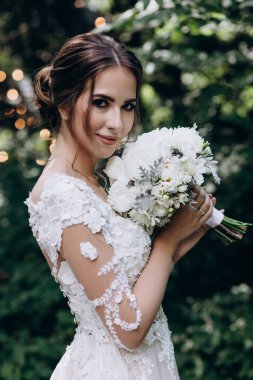Beyaz gelinlik içinde, elinde buketle dışarıda bekleyen güzel bir gelin.     