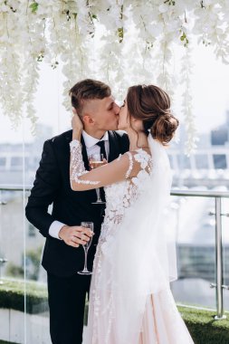 Düğün töreninde ellerinde şampanya bardakları ve öpüşen güzel bir çift. 