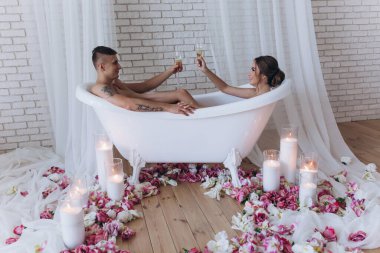 Birbirine aşık genç bir çift şampanya içiyor ve birlikte banyonun tadını çıkarıyor.                          