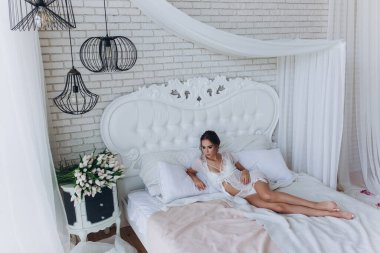 Yatak odasında poz veren çekici genç bir kadın. Gelinin sabahı       