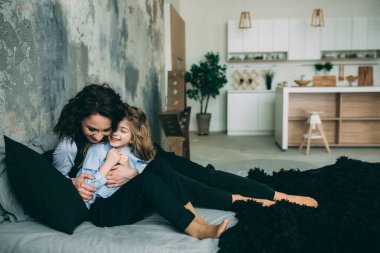 Stüdyo odasında yatakta poz veren genç mutlu anne ve kız. 
