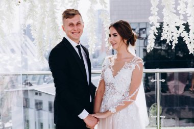 Mutlu genç gelin ve damat el ele tutuşup düğün töreninde gülümsüyor.