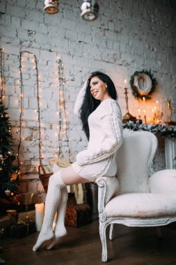 Genç ve seksi bir kadın, kumral saçlı rahat bir Noel arifesinde poz veriyor.           