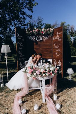 Güzel, mutlu gelin ve damat açık hava düğün töreninde ellerinde mumlar ve çiçeklerle masada oturuyorlar..              