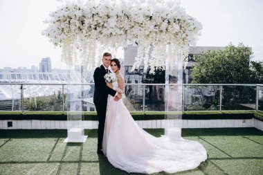 Düğün kemeri ve şehrin arka planında sarılan mutlu gelin ve damat.