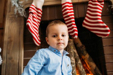 Küçük çocuk Noel süslü şöminenin yanında oturuyor. 