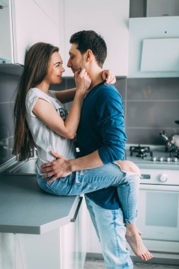 Güzel, genç, sevgi dolu bir çift mutfakta sarılıyor.    