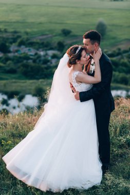 Mutlu evlilik çifti doğada sarılıp öpüşüyor.