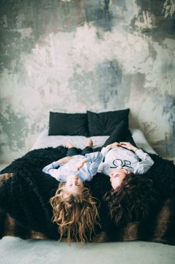 Stüdyo odasında yatakta poz veren genç mutlu anne ve kız. 