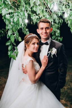 Gelin ve damat geceleri dışarıda kameralara sarılıp gülümsüyor.