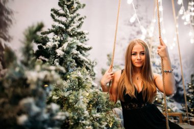 Stüdyodaki kız Noel süsleriyle salıncakta sallanıyor. Yeni yıl arifesi