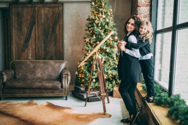 Mutlu anne ve küçük kızı Noel için dekore edilmiş stüdyoda poz veriyorlar.