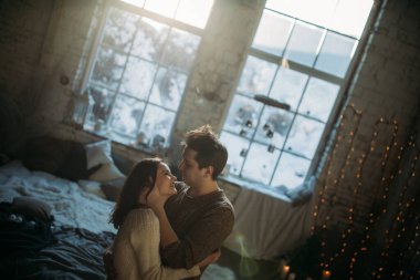 Genç çift yatakta oturuyor ve sarılıyorlar. 