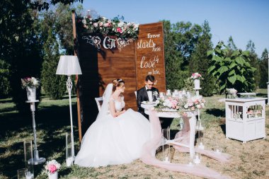 Güzel, mutlu gelin ve damat açık hava düğün töreninde ellerinde mumlar ve çiçeklerle masada oturuyorlar..              