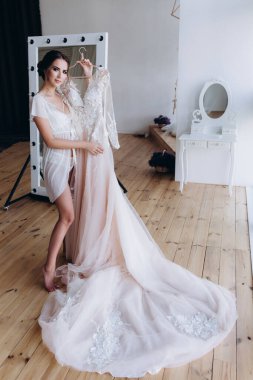 Çekici genç gelin sabah zarif bir gelinlik tutuyor.   