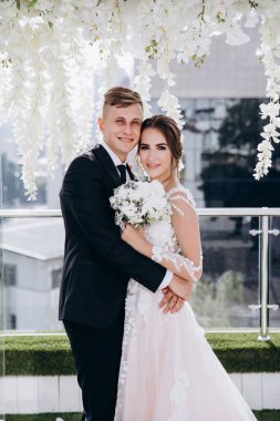 Güzel genç gelin ve damat kameraya sarılıp gülümsüyor.