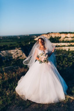 Gün batımında dışarıda poz veren gelinlik içinde güzel, mutlu bir gelin.