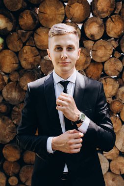 Siyah takım elbiseli ve kravatlı, kameraya gülümseyen yakışıklı bir gencin portresi.