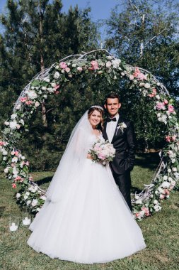 Güzel, mutlu gelin ve damat, düğün günlerinde çiçek kemerinin yanında.    