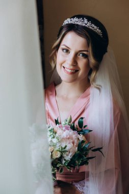 Pembe ipek bornoz ve duvak içinde güzel bir gelin Sabah düğün buketi tutuyor            