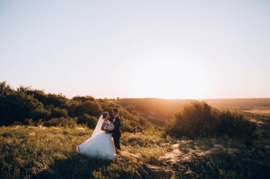 Mutlu gelin ve damat gün batımında güzel bir manzarada yürüyorlar.                
