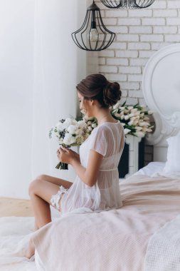 Güzel genç bir kadın sabah yatak odasında bir buket çiçek tutuyor.                      