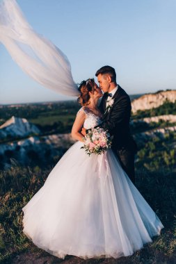 Mutlu gelin ve damat gün batımında güzel bir manzarada yürüyorlar.                