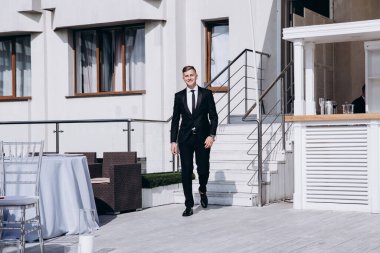 Terasta yürüyen takım elbiseli yakışıklı genç adam.