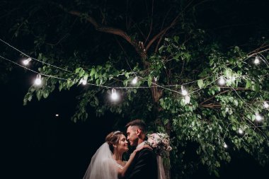 Güzel bir çift yeni evli gece ağacın yanında poz veriyor.