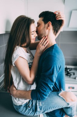 Genç çift mutfakta sarılıp öpüşüyor..