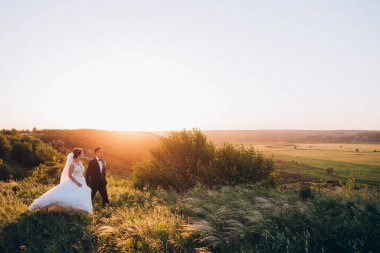 Mutlu gelin ve damat gün batımında güzel bir manzarada yürüyorlar.                