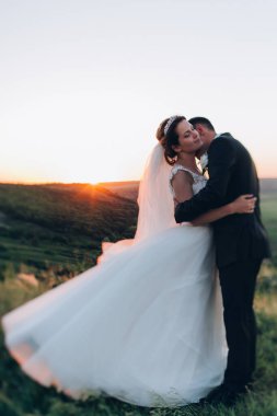 Mutlu gelin ve damat gün batımında güzel bir manzarada yürüyorlar.                