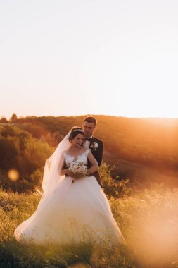 Mutlu gelin ve damat gün batımında güzel bir manzarada yürüyorlar.                