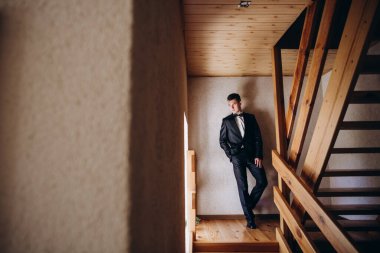 Ahşap merdivenlerde poz veren şık takım elbiseli yakışıklı genç adam. 