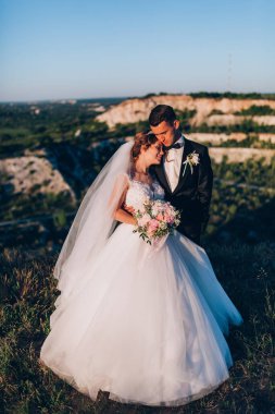 Mutlu gelin ve damat gün batımında güzel bir manzarada yürüyorlar.                