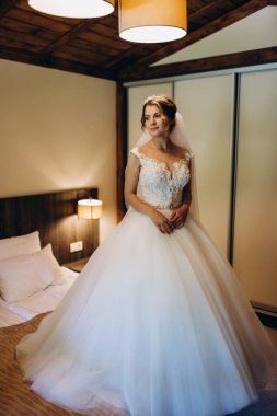 Beyaz gelinlik ve duvak içinde güzel genç gelin sabah evde poz veriyor.       
