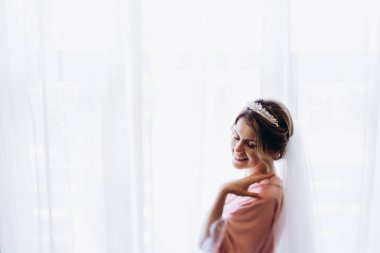 Beyaz gelinlik ve duvak içinde güzel genç gelin sabah evde poz veriyor.       
