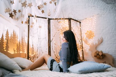 Odada, çelenklerle süslenmiş bir yatakta poz veren kadın. 