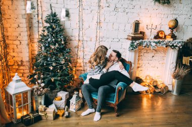 Birbirine aşık mutlu genç çift rahat bir odada Noel ağacının yanında oturuyor.           