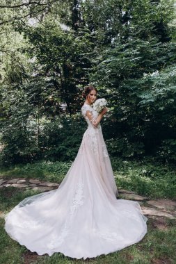 Beyaz gelinlik içinde, elinde buketle dışarıda bekleyen güzel bir gelin.     