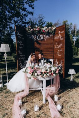 Güzel, mutlu gelin ve damat açık hava düğün töreninde ellerinde mumlar ve çiçeklerle masada oturuyorlar..              