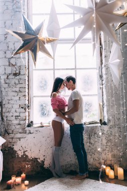 Yeni yıl dekorunda mutlu çift pencerenin yanında poz veriyor 