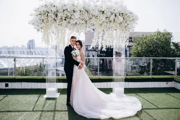 Düğün kemeri ve şehrin arka planında sarılan mutlu gelin ve damat.