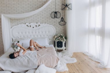 Beyaz dantelli iç çamaşırlı güzel bir kadın ve sabah yatak odasında bir buket düğün çiçeği.              