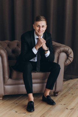 Şık takım elbiseli yakışıklı bir gencin portresi koltukta oturuyor.